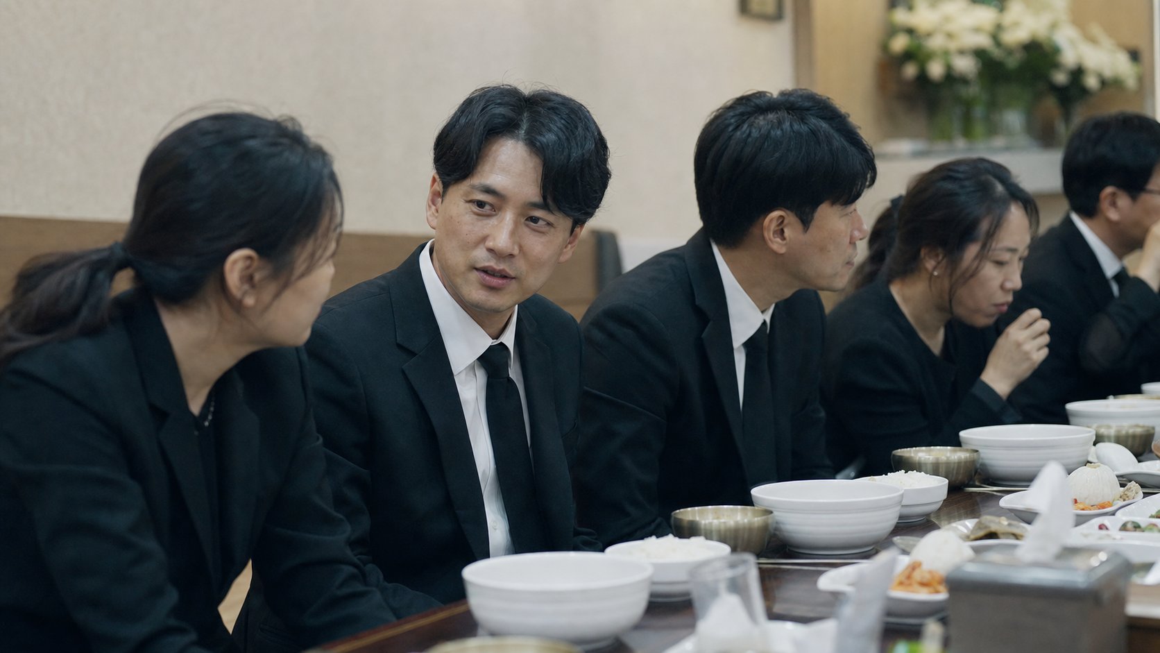 장례식장 접객실에서 조용히 식사하는 검정 정장 조문객들