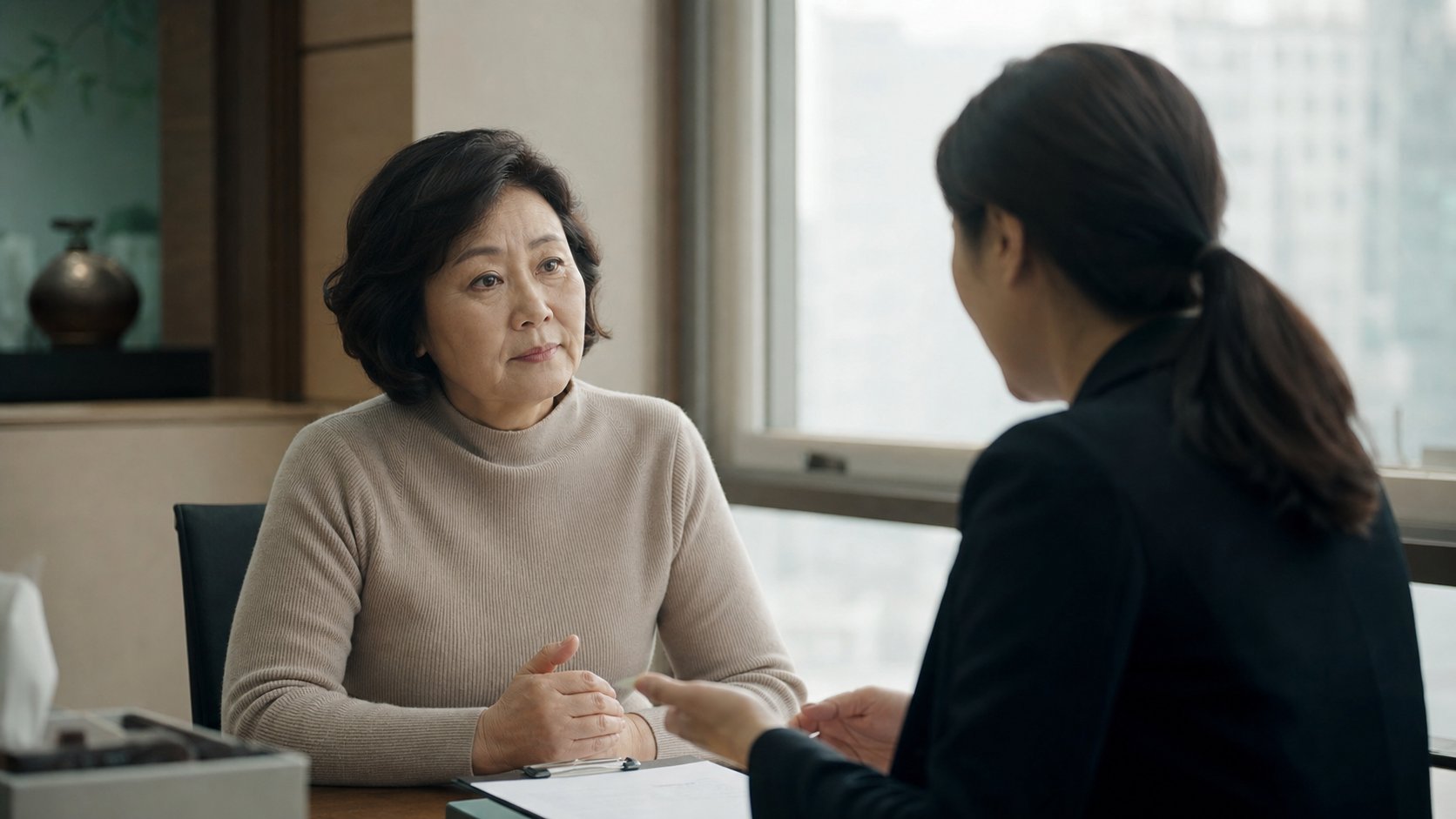 사무실 창가에서 상담원과 상조 상품 유지 방안을 의논하는 중년 여성