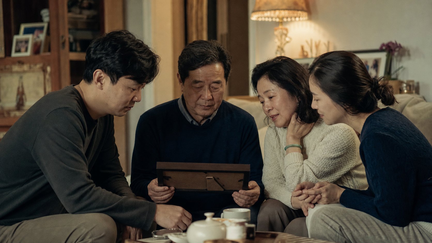 따뜻한 거실에서 가족이 함께 모여 고인의 사진을 보며 잔잔히 추억을 나누는 평온한 장면