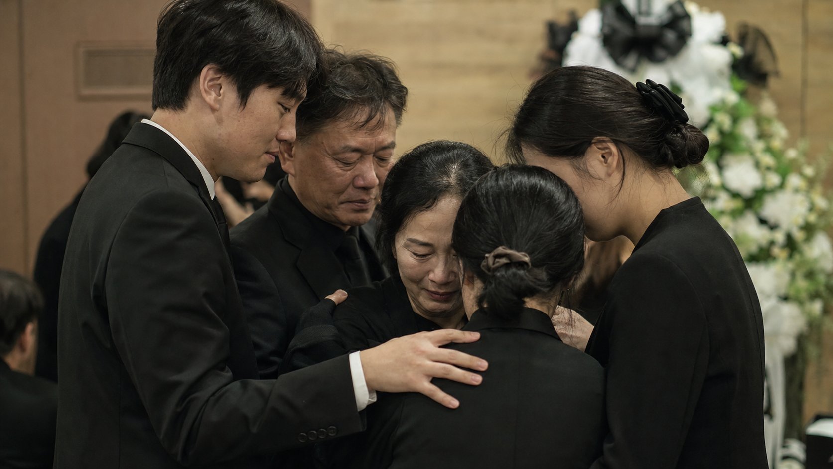 가족이 빈소 한쪽에 모여 앉아 서로를 위로하며 조용히 슬픔을 나누는 차분한 장면
