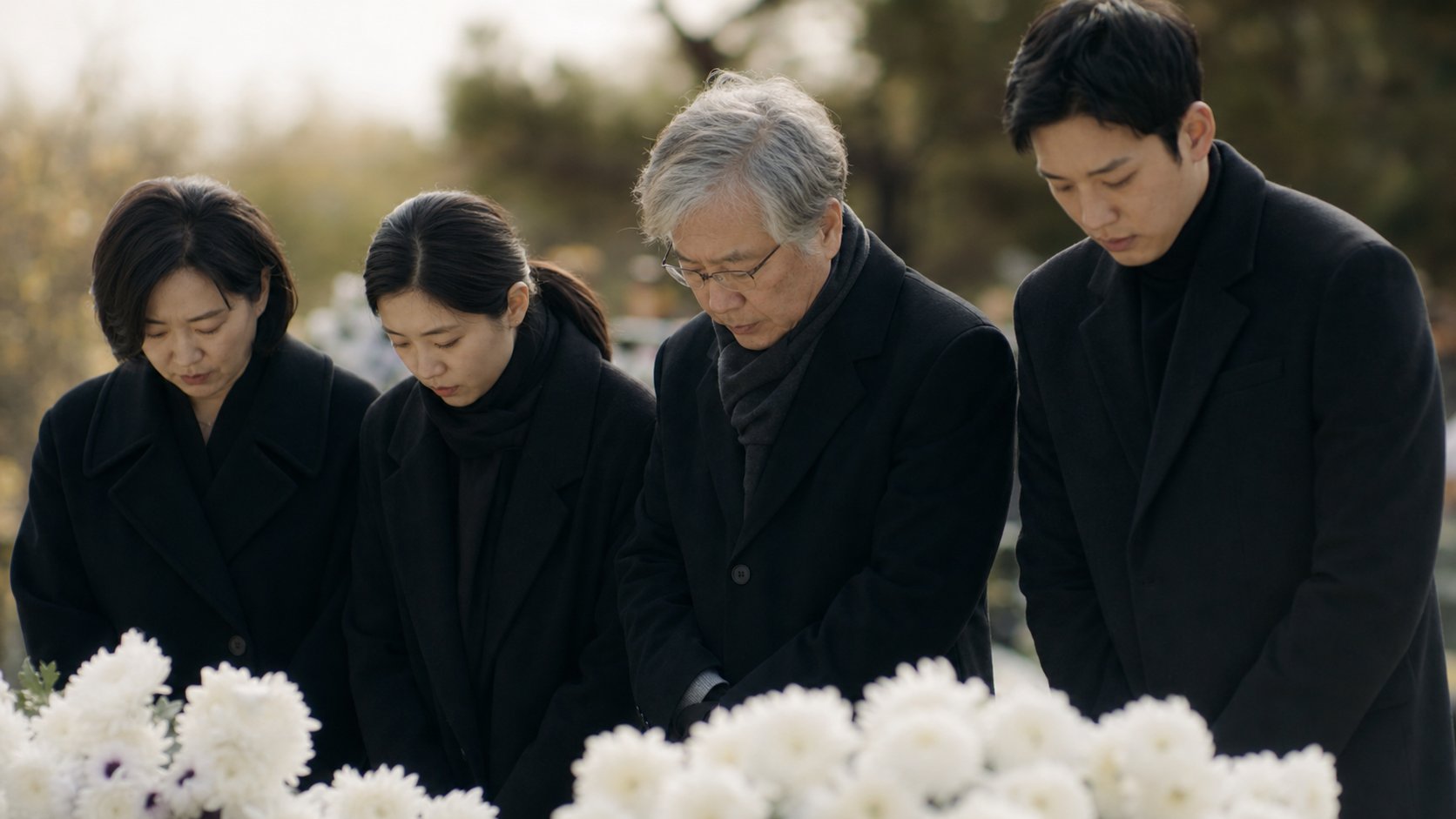장사를 마친 가족이 흰 국화 앞에서 묵념하며 추모하는 장면