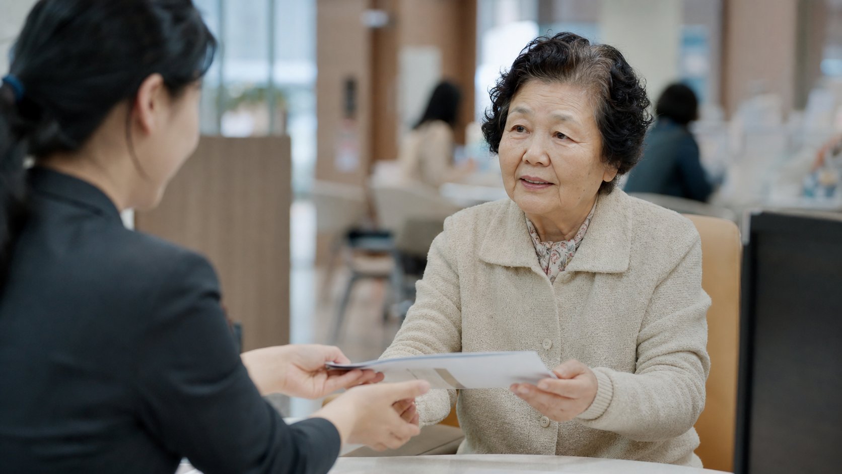 상담 직원에게 서류를 건네받으며 설명을 듣는 노년 여성